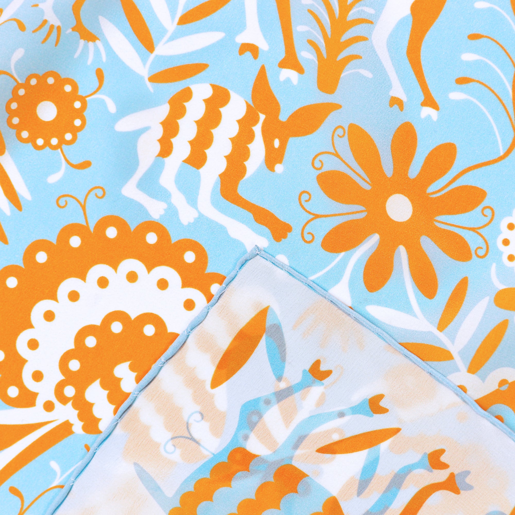 Detail of the Noé Miroir silk scarf showing hand-painted animal and botanical motifs and the hand-rolled hem.