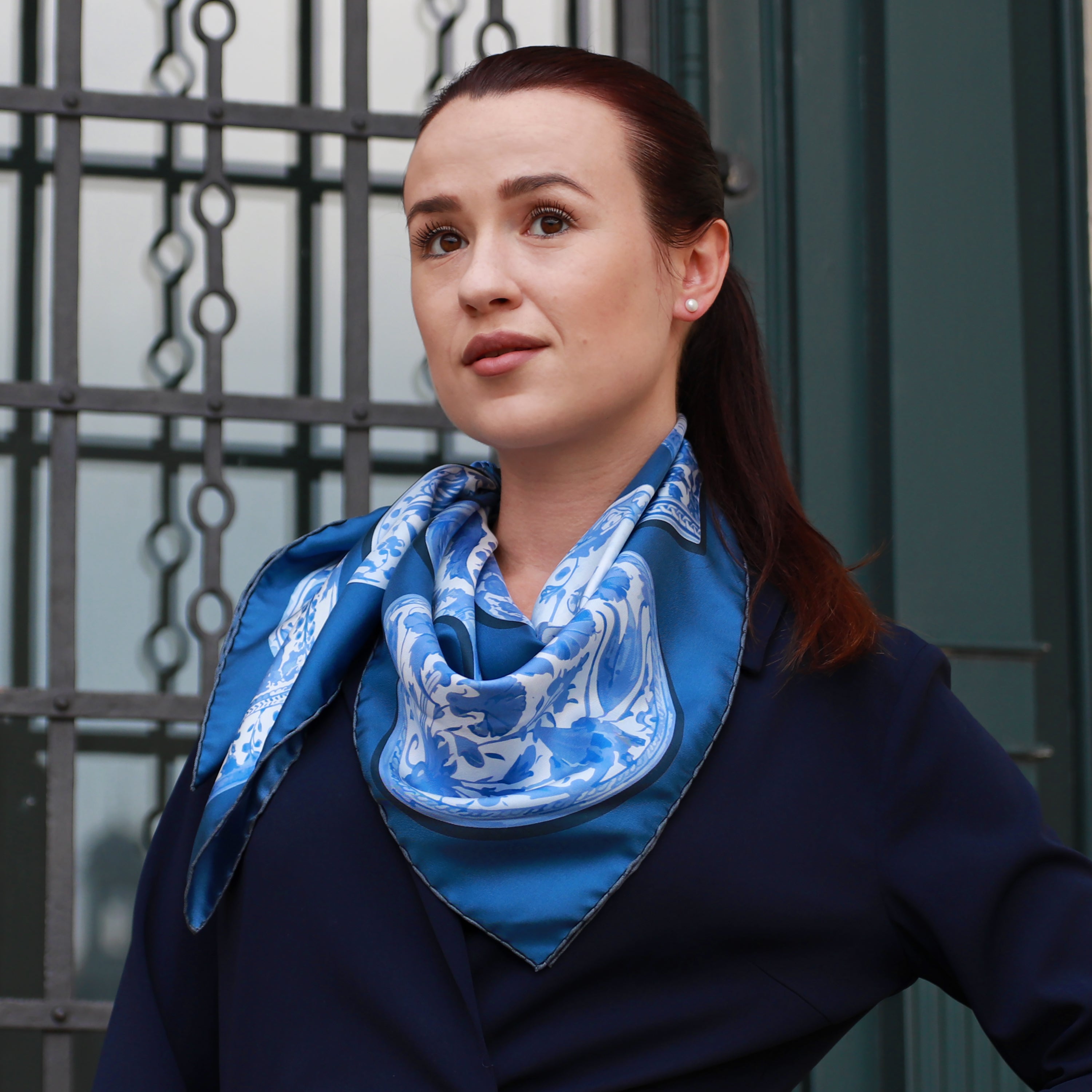 Model wearing the Iznik Marian double-sided silk scarf styled around the neck with a navy blazer.