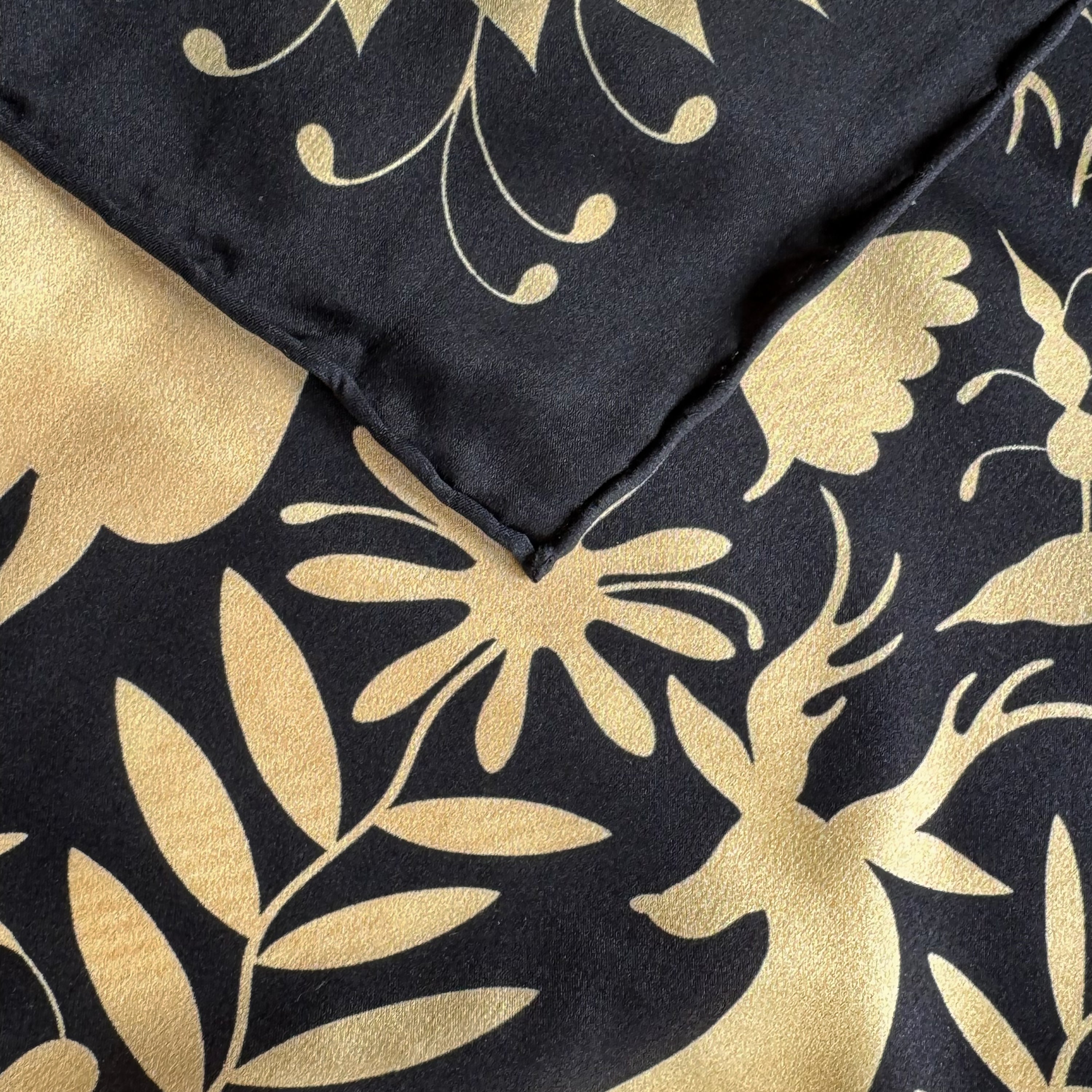 Detail of the Noé Gold silk scarf showing hand-painted animal and botanical motifs and the hand-rolled hem.