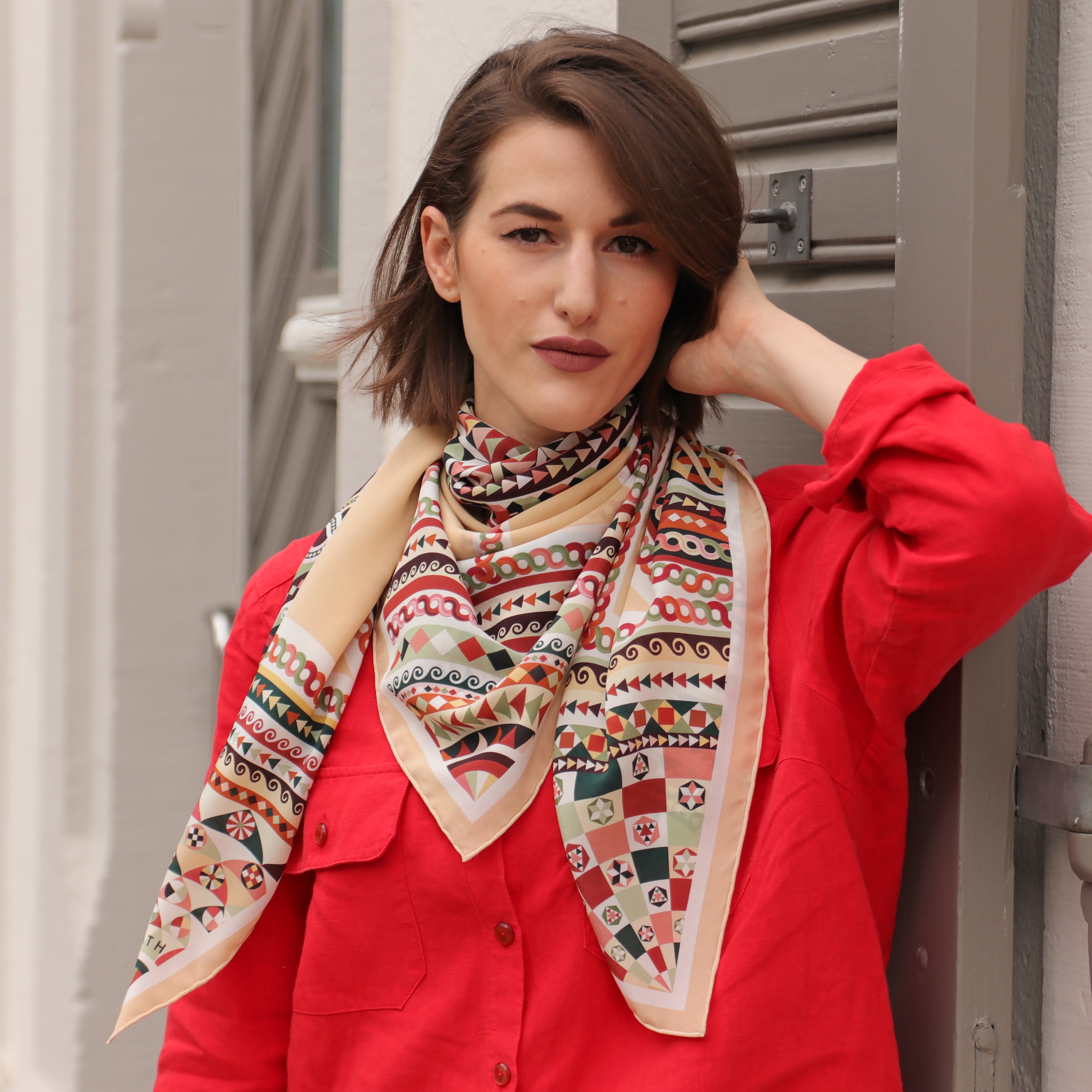 Model wearing the Basilica Rena silk scarf styled around the neck with a red blouse.