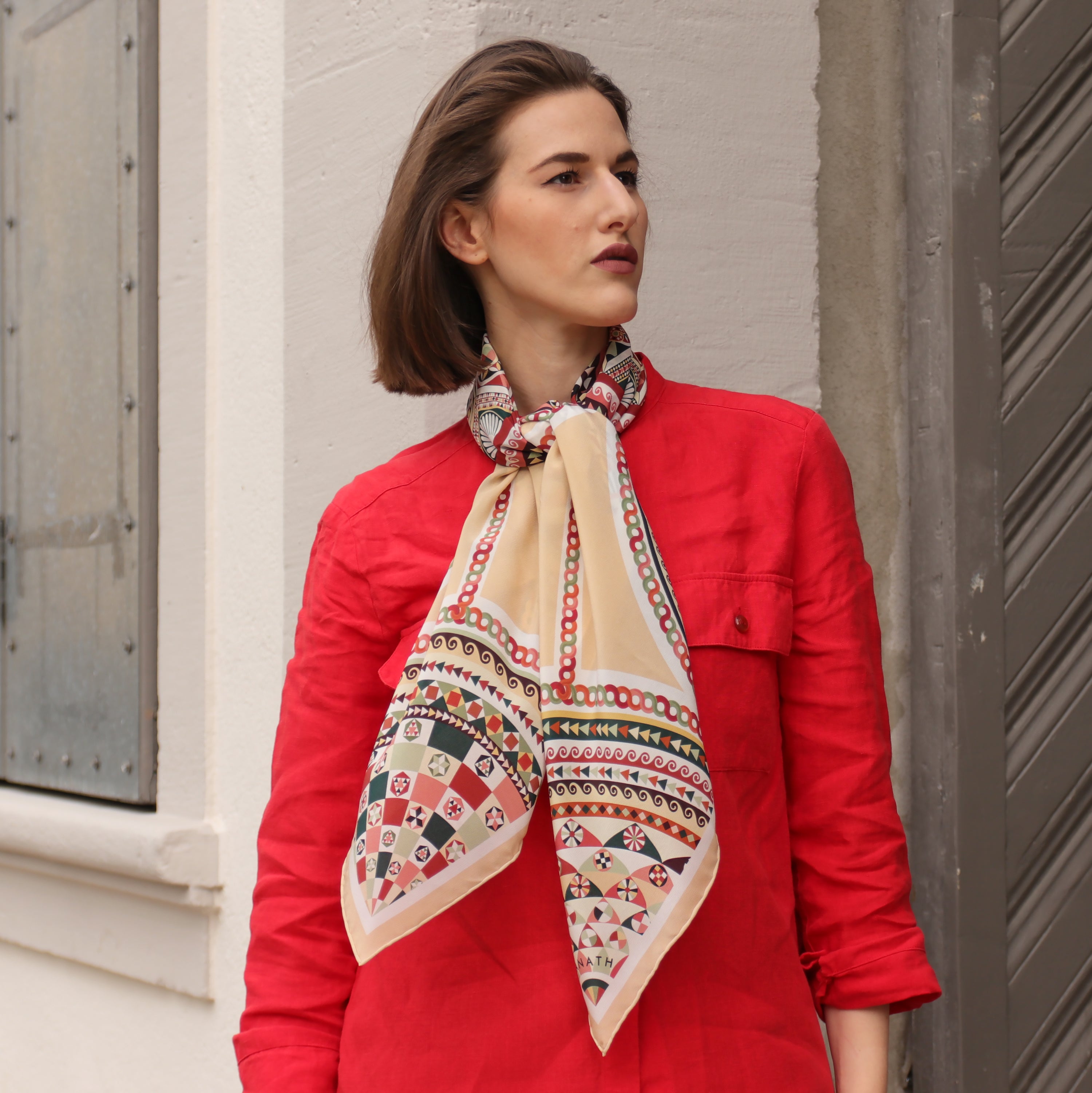 Model wearing the Basilica Rena silk scarf styled around the neck with a red jacket.