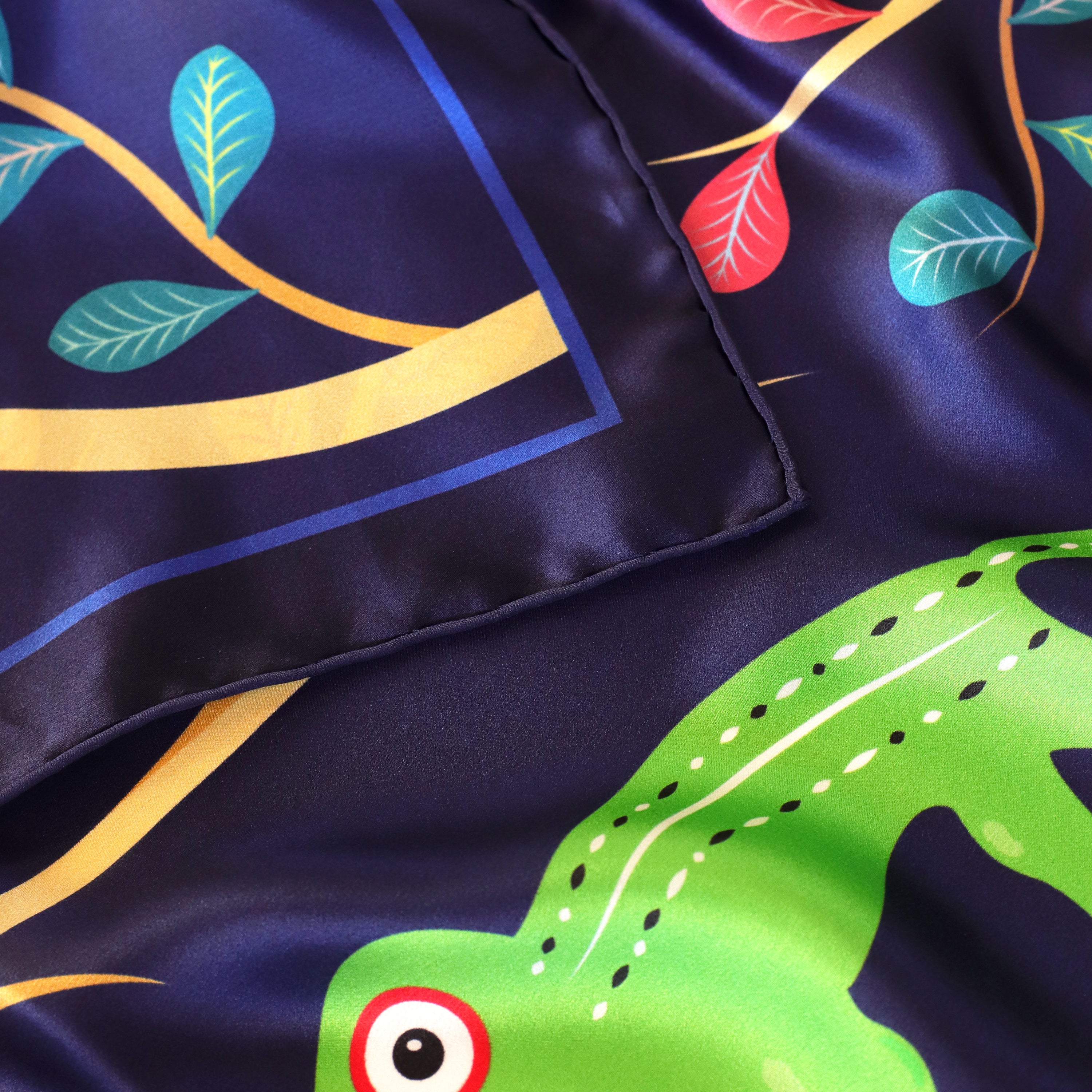 Detail of the Abomey Indigo silk scarf showing hand-painted animal and botanical motifs and the hand-rolled hem.