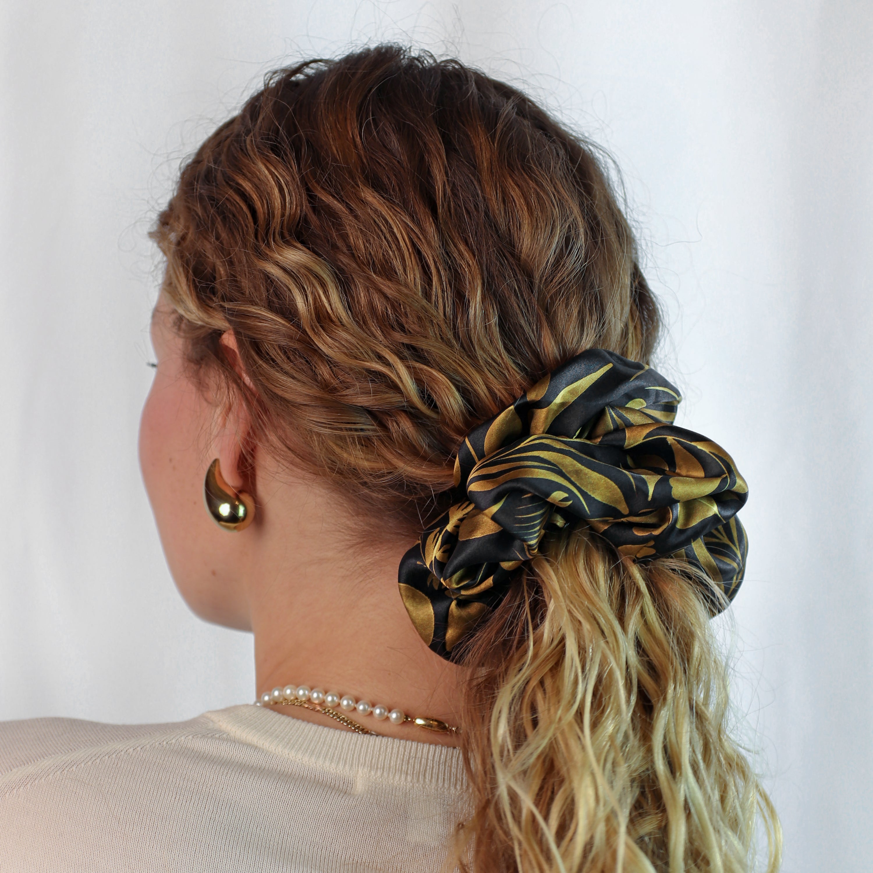 Model wearing the Foglie d'Oro giant silk scrunchie in the hair, featuring a botanical leaf motif in gold and black on 100% silk satin.