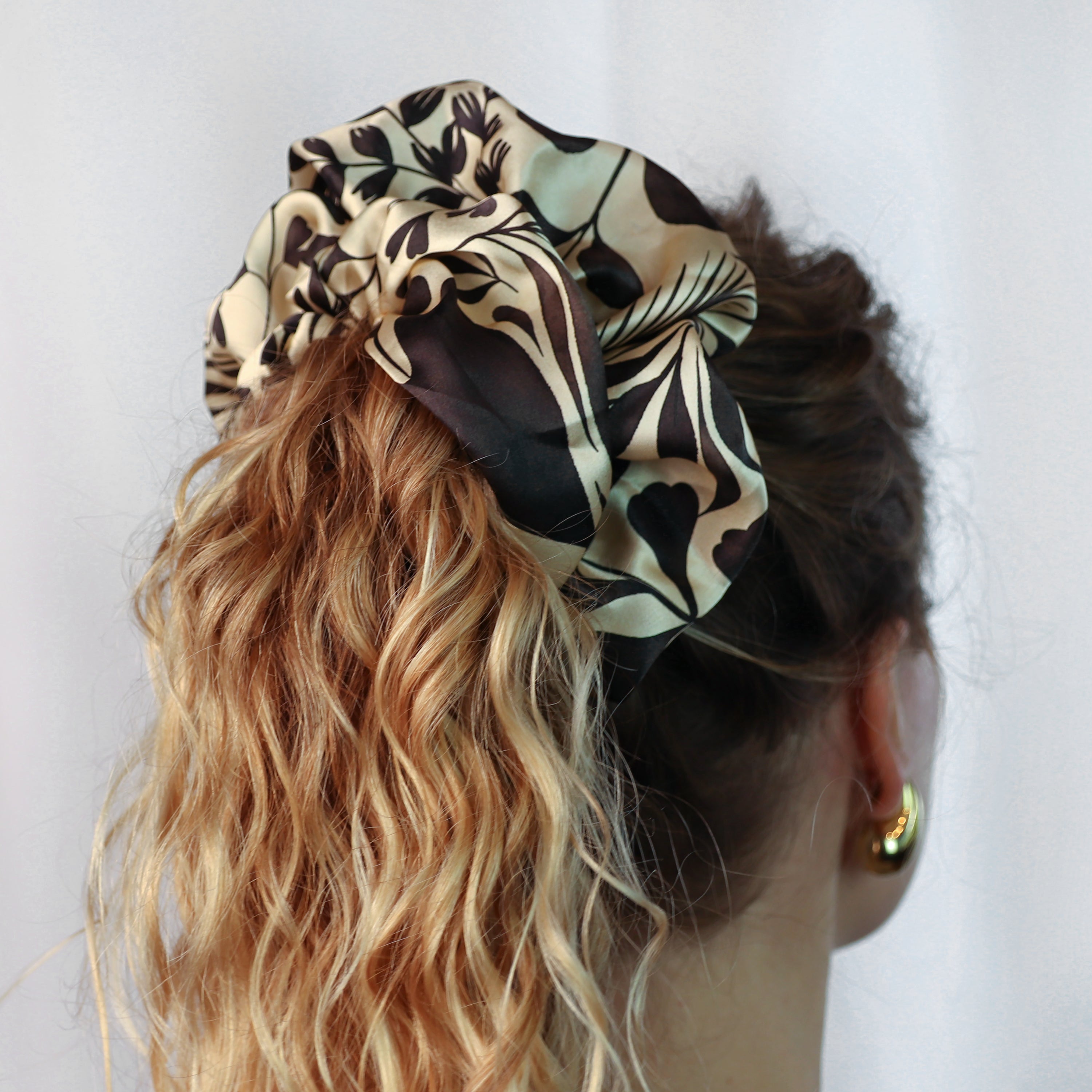 Model wearing the Foglie Crema giant silk scrunchie in the hair, featuring a botanical leaf motif in ivory and black on 100% silk satin.