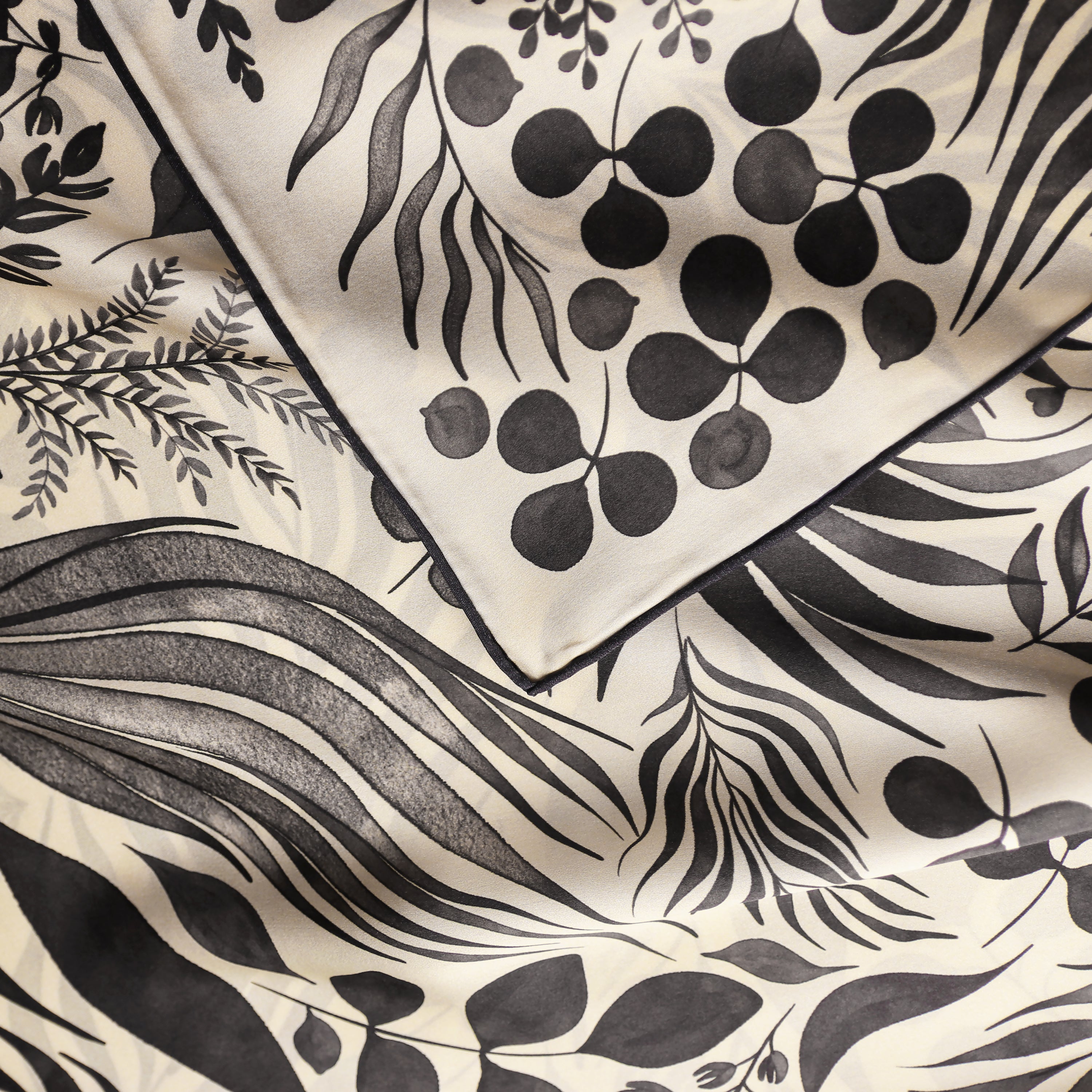 Detail of the Foglie Crema silk scarf showing hand-painted botanical leaf motifs and the hand-rolled hem.