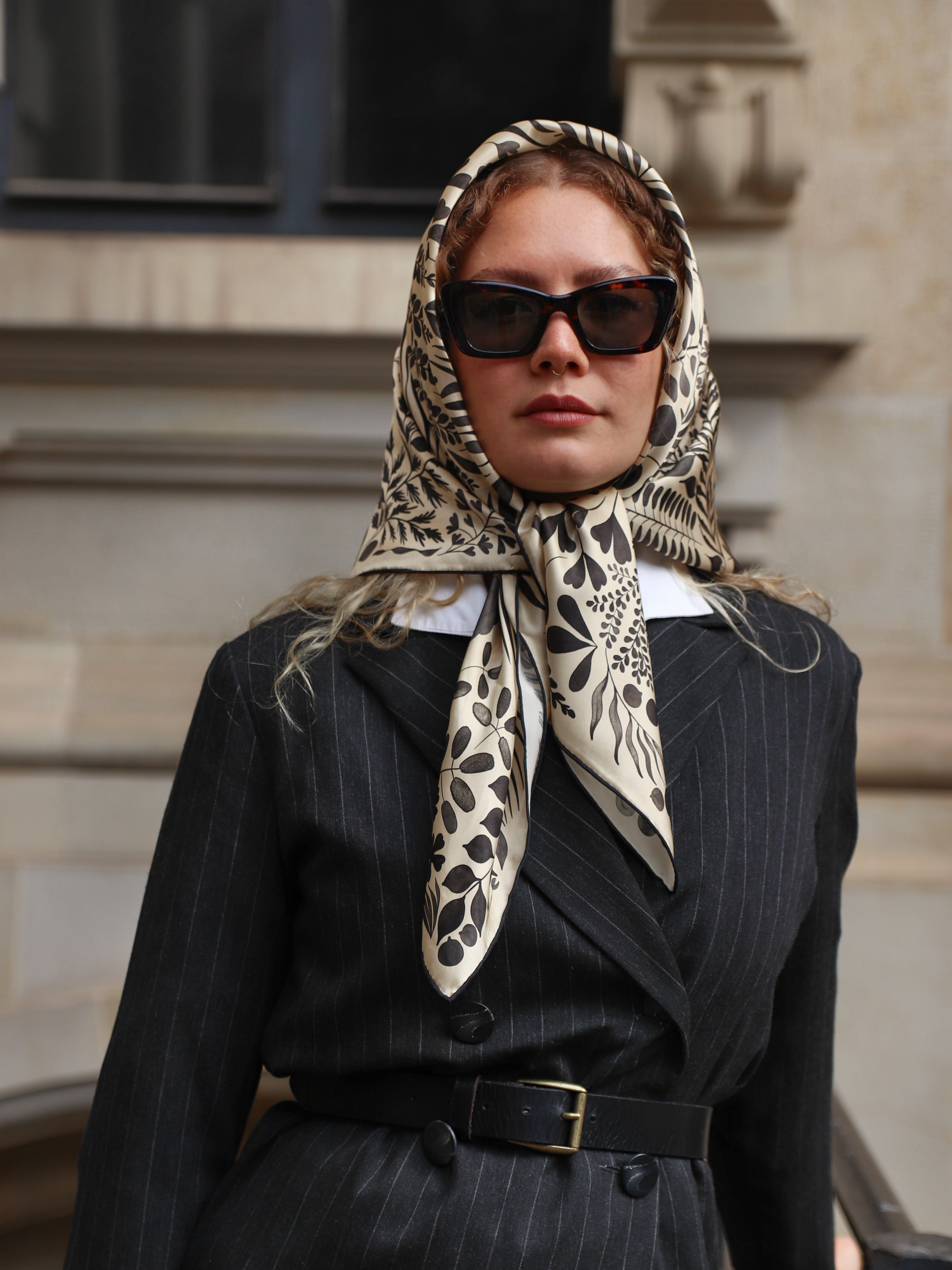 Model wearing the Foglie Crema silk scarf styled as a headscarf with a black blazer.
