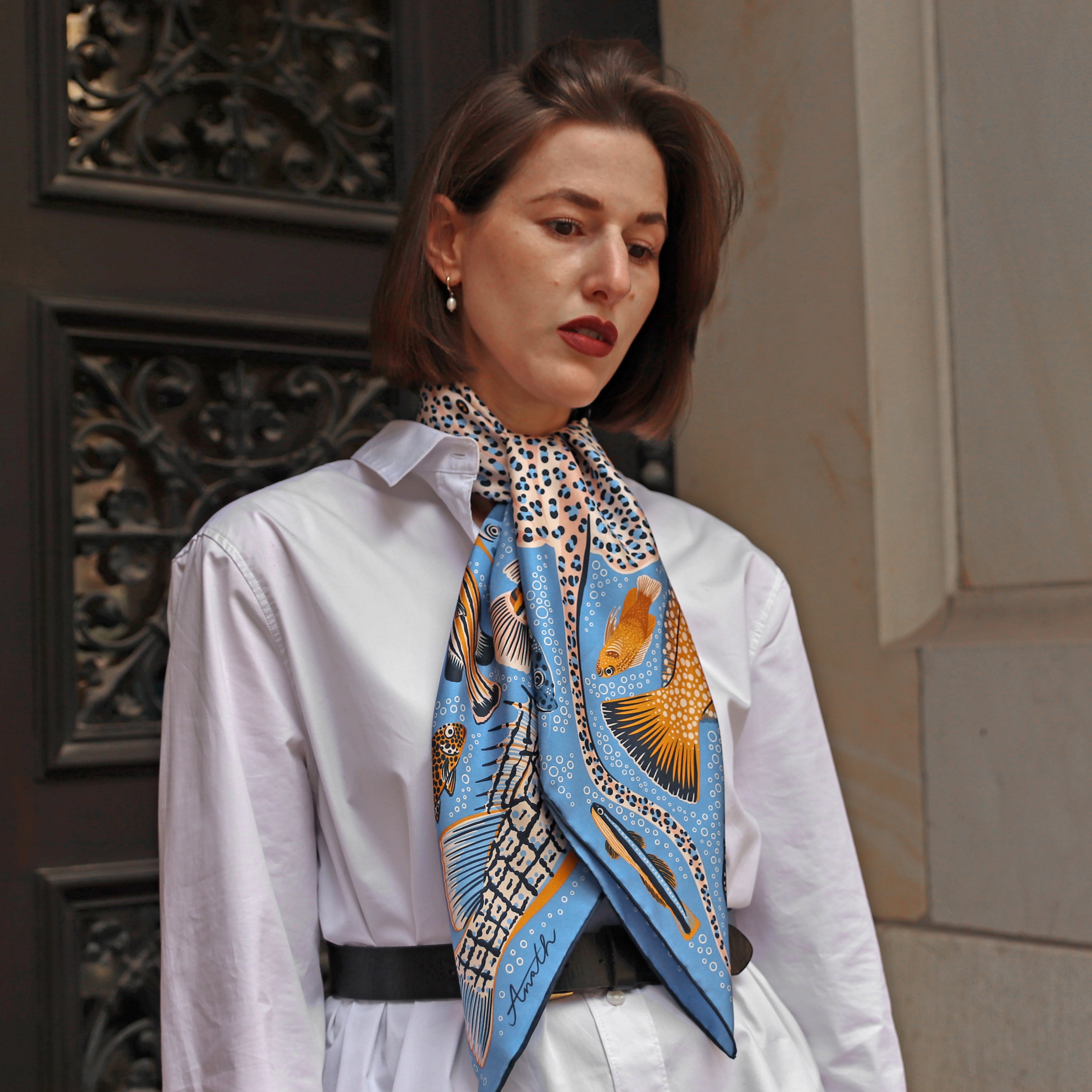 Model wearing the Pesce Iris double-sided silk scarf styled as a neck scarf with a white shirt.