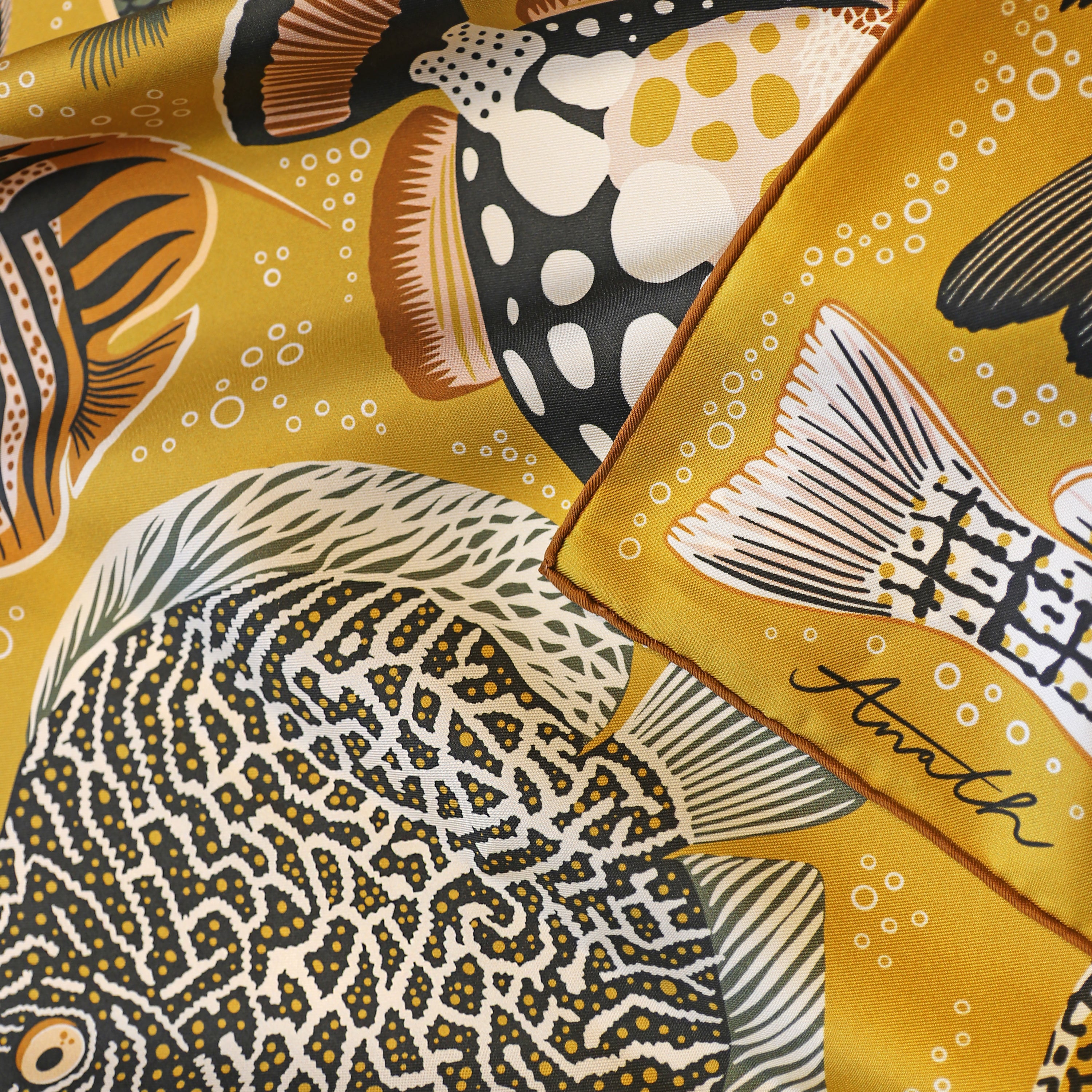 Close-up detail of the Pesce Miele double-sided silk scarf showing the hand-rolled hem and hand-painted fish illustrations on 100% silk twill.