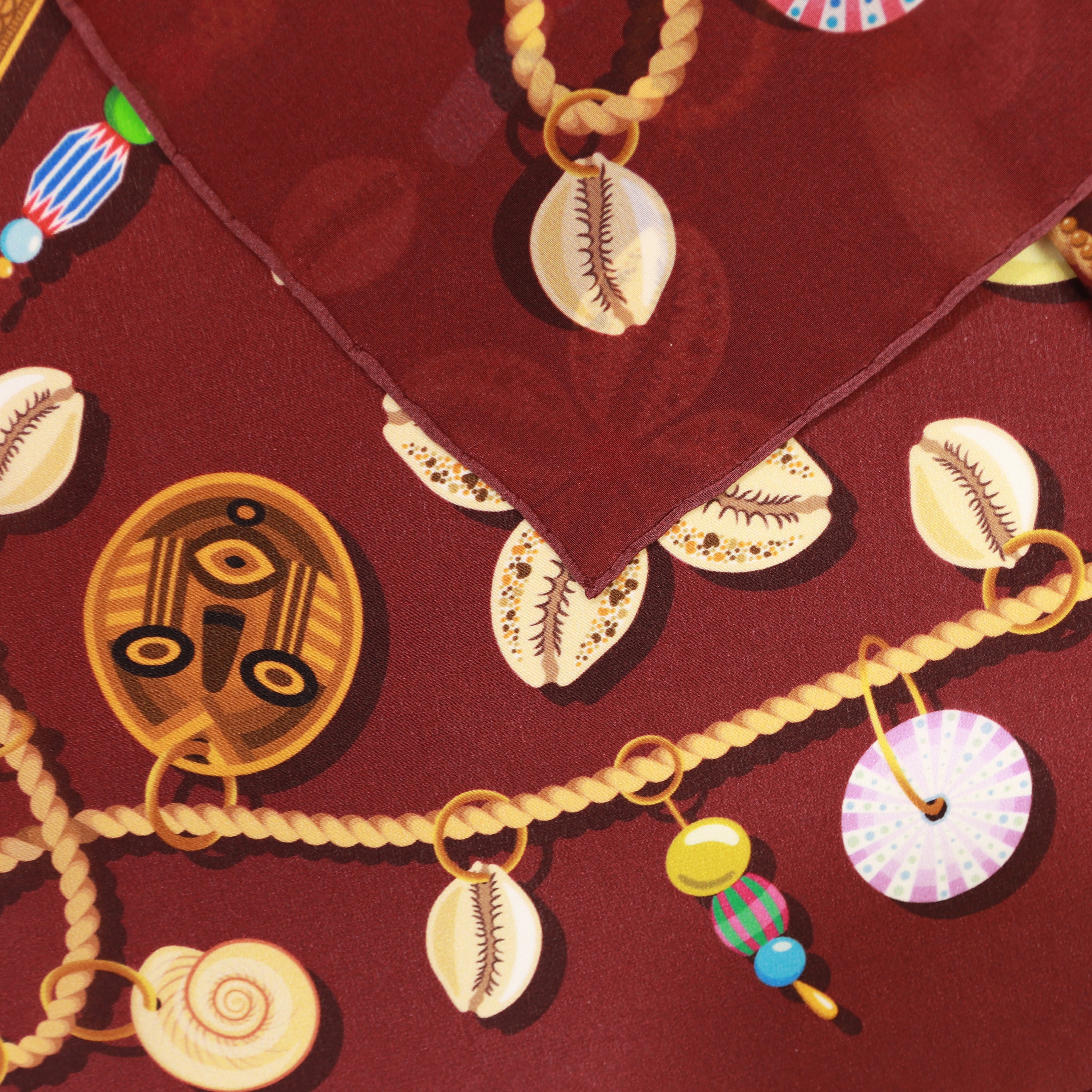 Detail of the Kauri Rubis silk bandana scarf showing hand-painted cowrie shell, chain and spiral motifs.