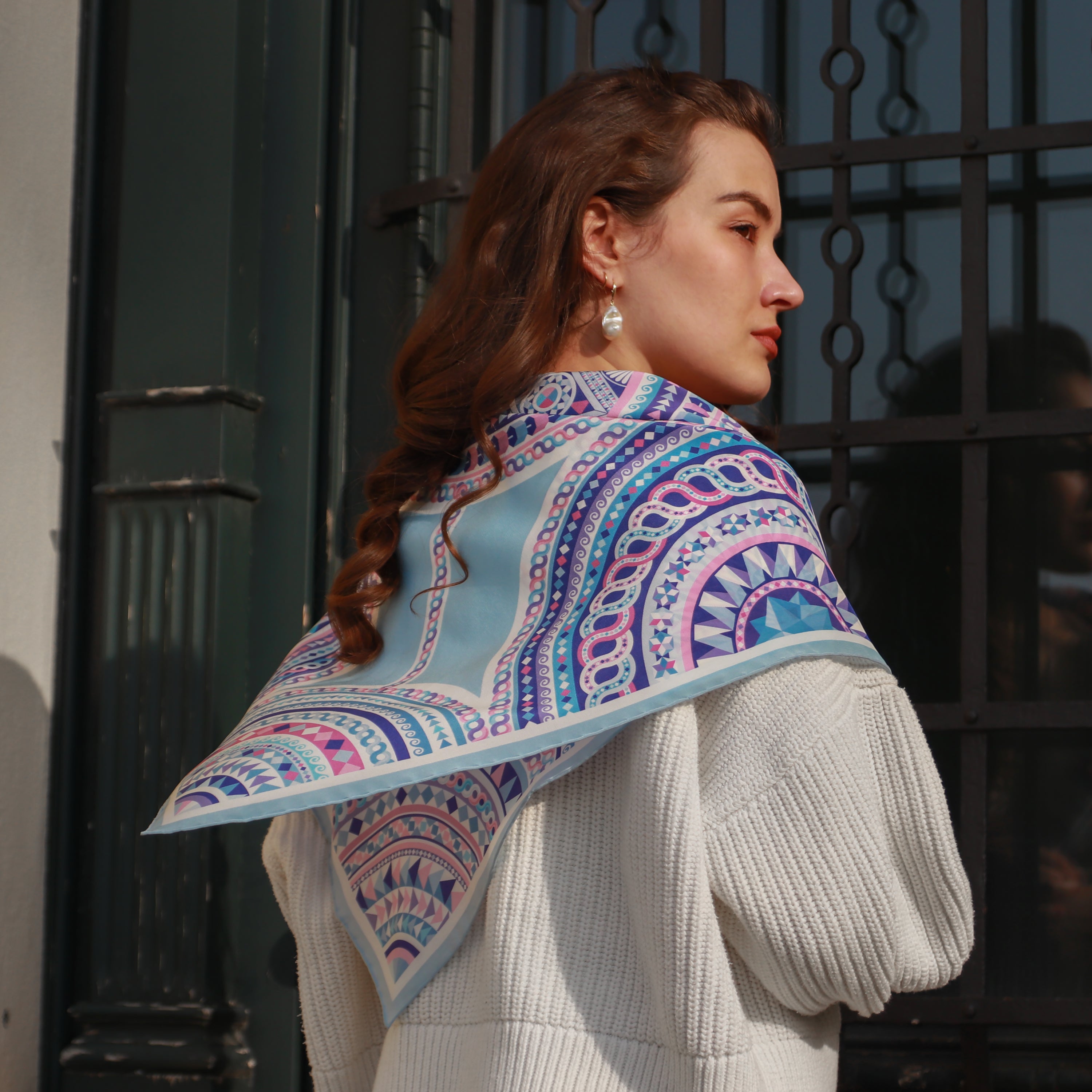 Model wearing the Basilica Zaffiro silk scarf draped over the shoulders with a white sweater.