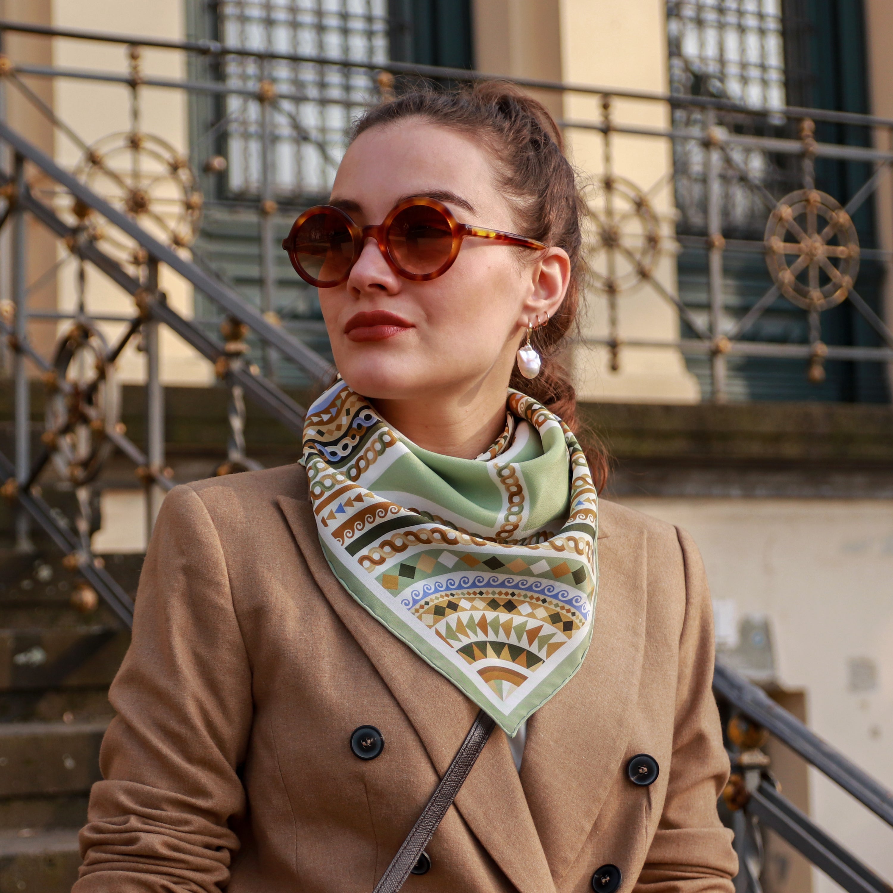 Model wearing the Basilica Giada silk scarf styled around the neck with a camel coat.