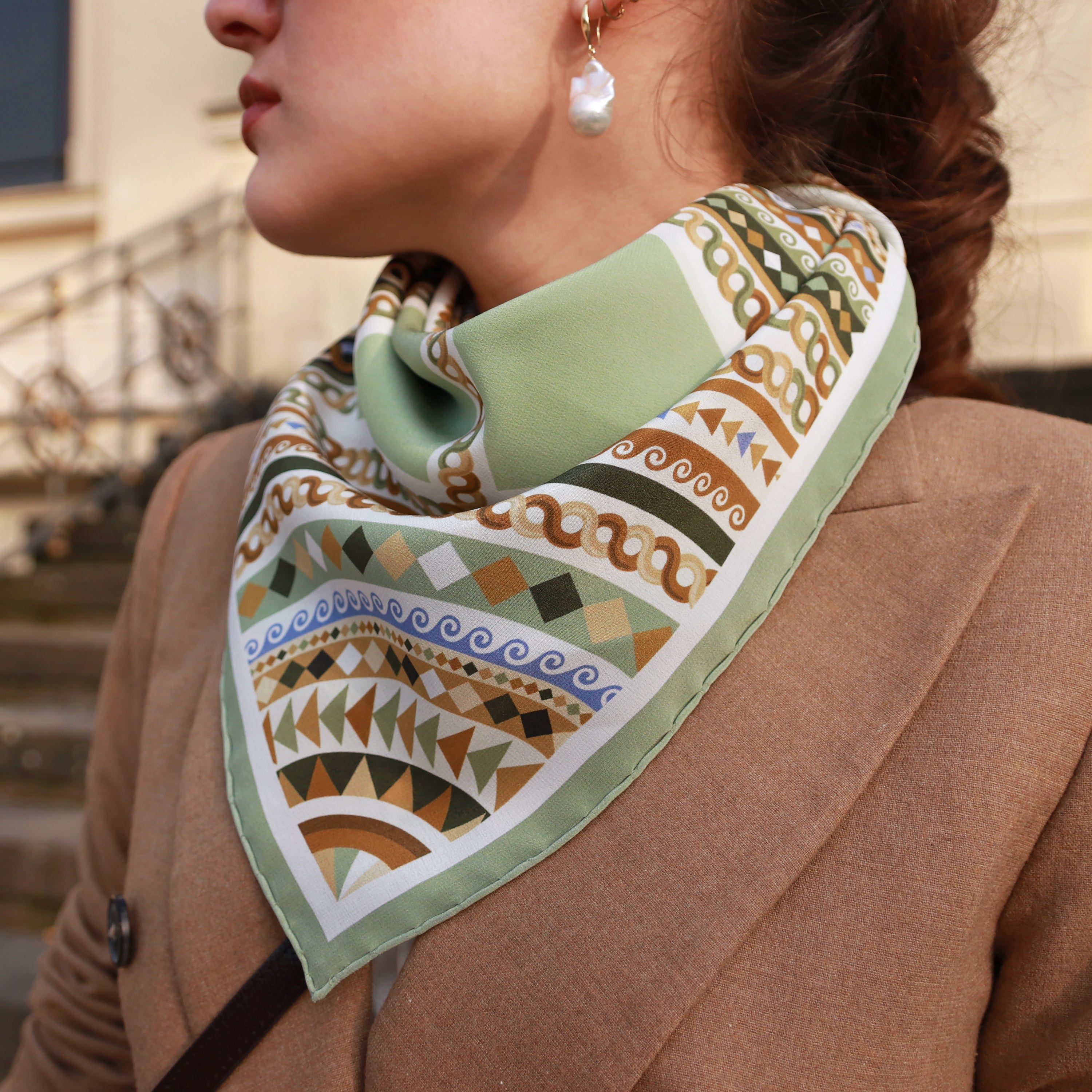 Model wearing the Basilica Giada silk scarf styled around the neck with a camel coat.