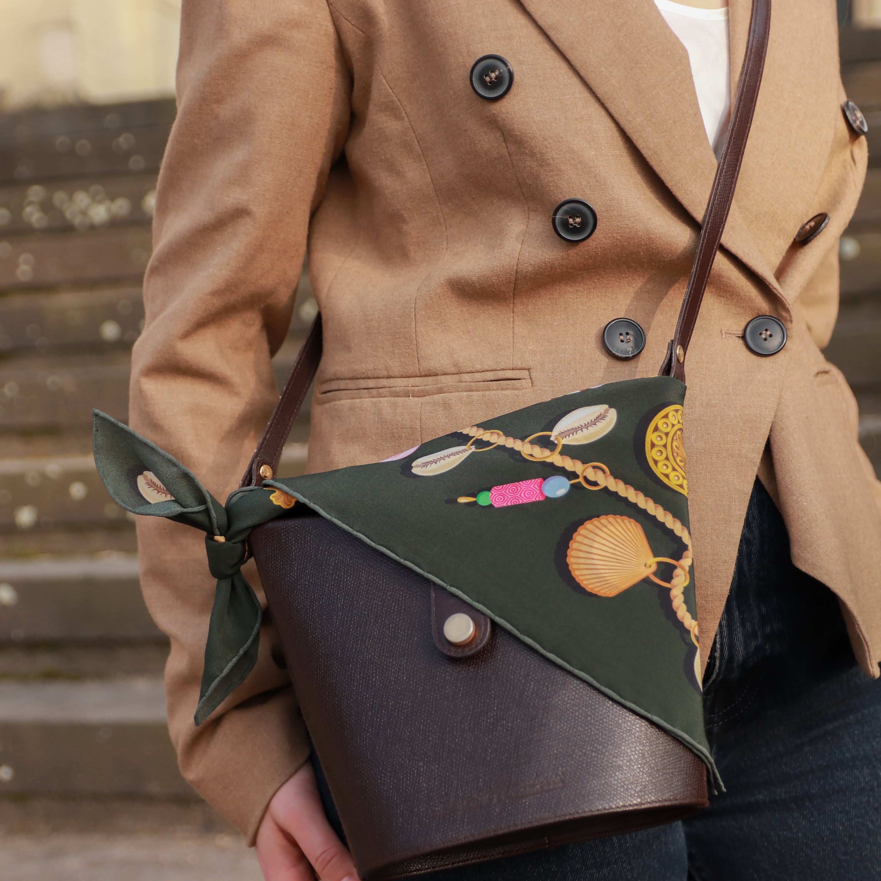 Model wearing the Kauri Delphine silk bandana scarf styled with a camel coat and leather shoulder bag.