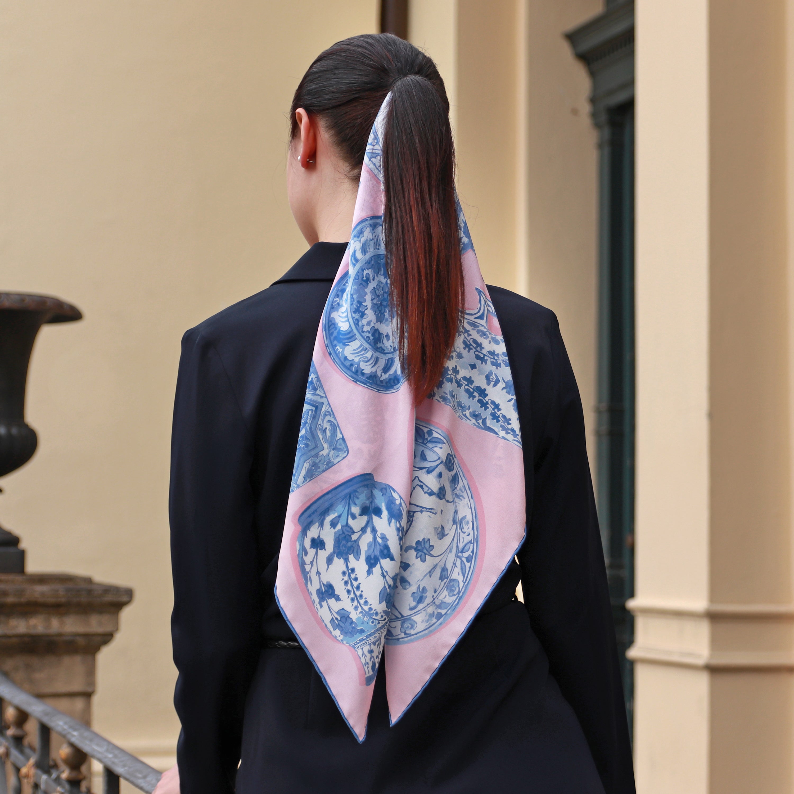 Model wearing the Iznik Rosé silk scarf draped down the back with a navy blazer.