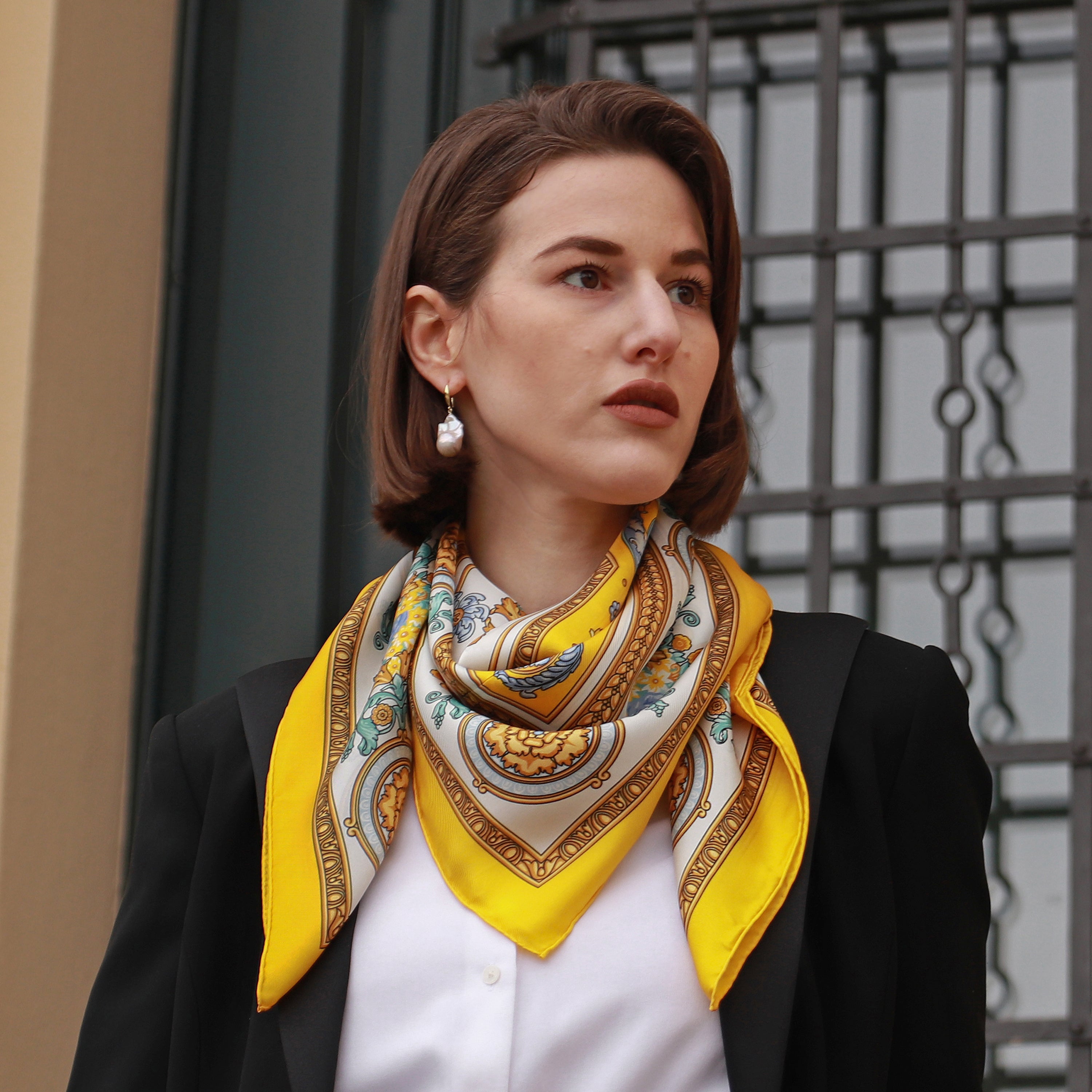 Model wearing the Rococo Limone silk scarf styled around the neck with a black blazer.