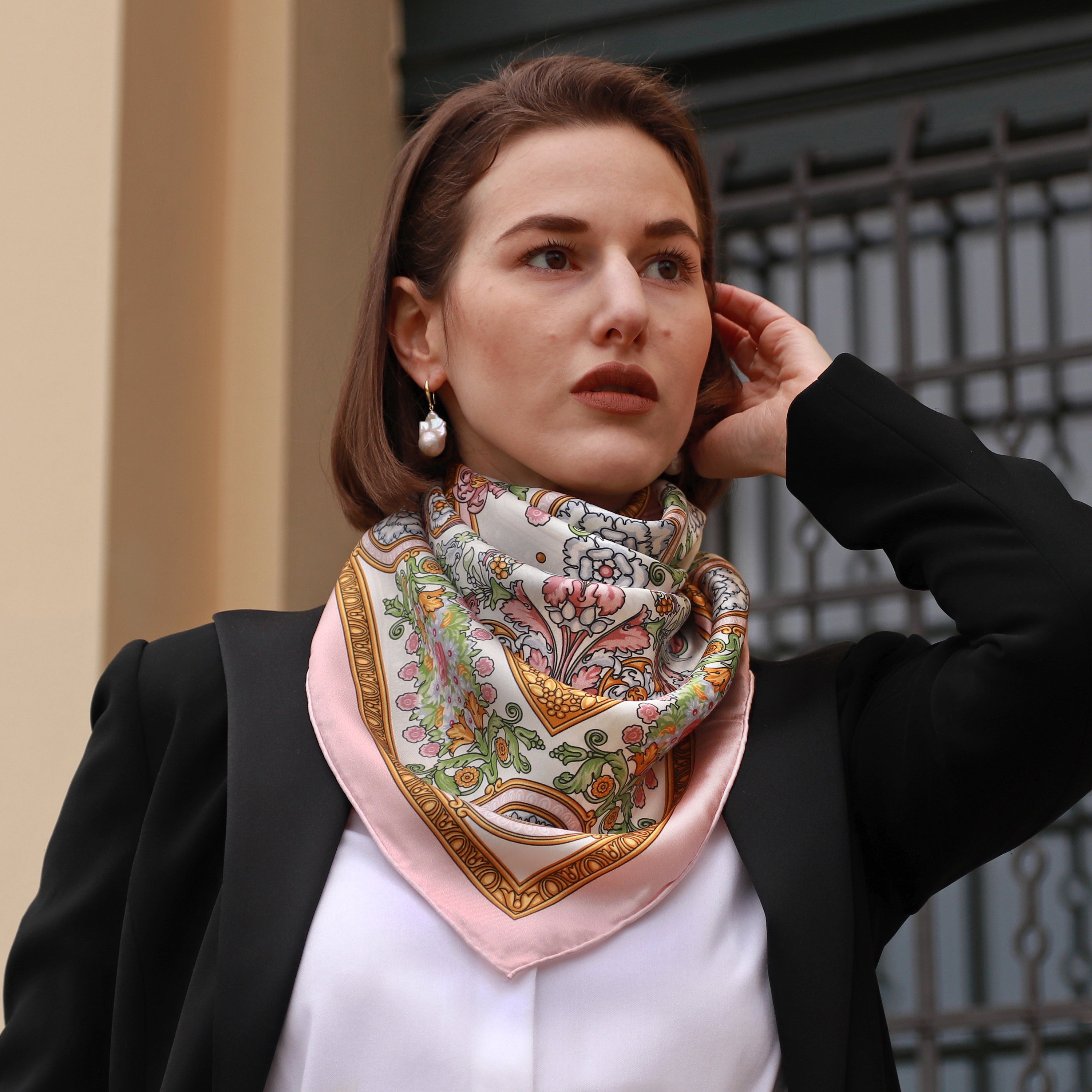 Model wearing the Rococo Rosa silk scarf styled around the neck with a black blazer and white blouse.
