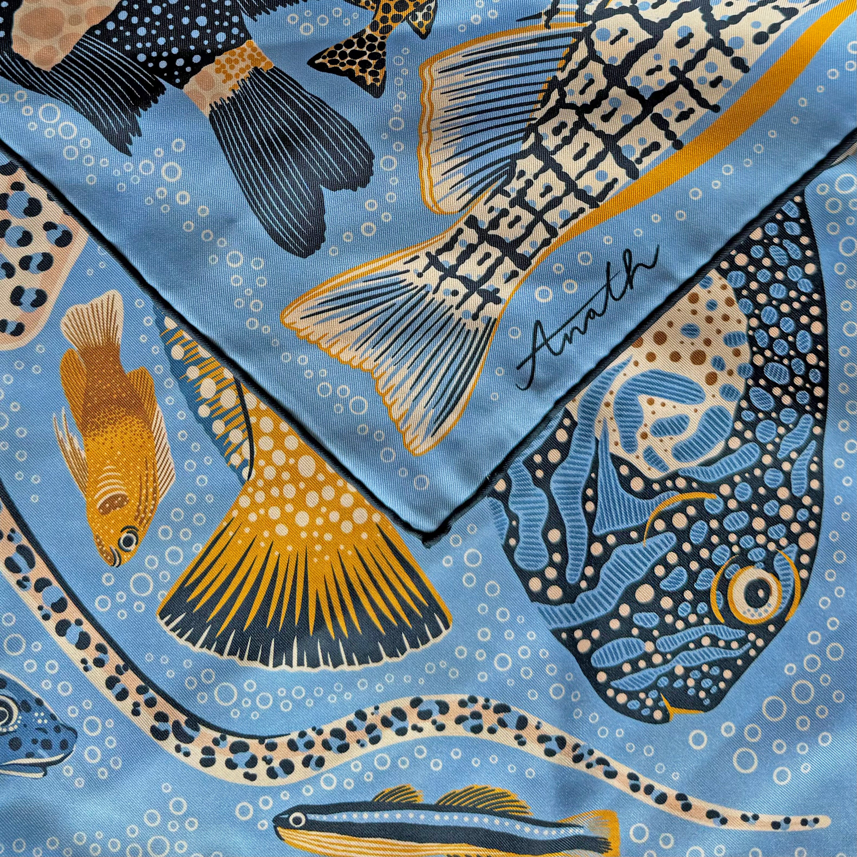 Detail of the Pesce Iris double-sided silk scarf showing the hand-rolled hem and cobalt blue fish motif on 100% silk twill.