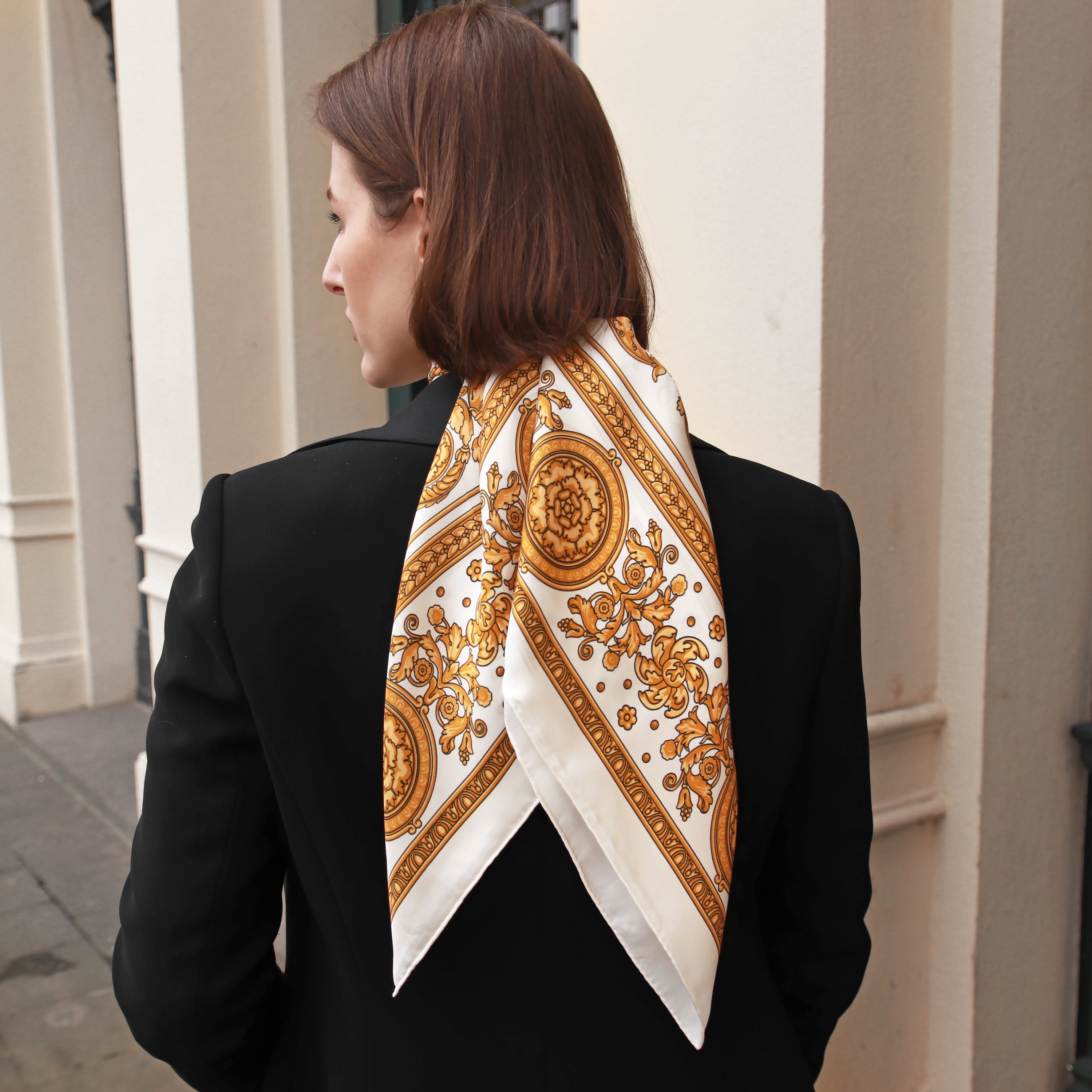 Model wearing the Rococo Natural silk scarf draped down the back with a black blazer.