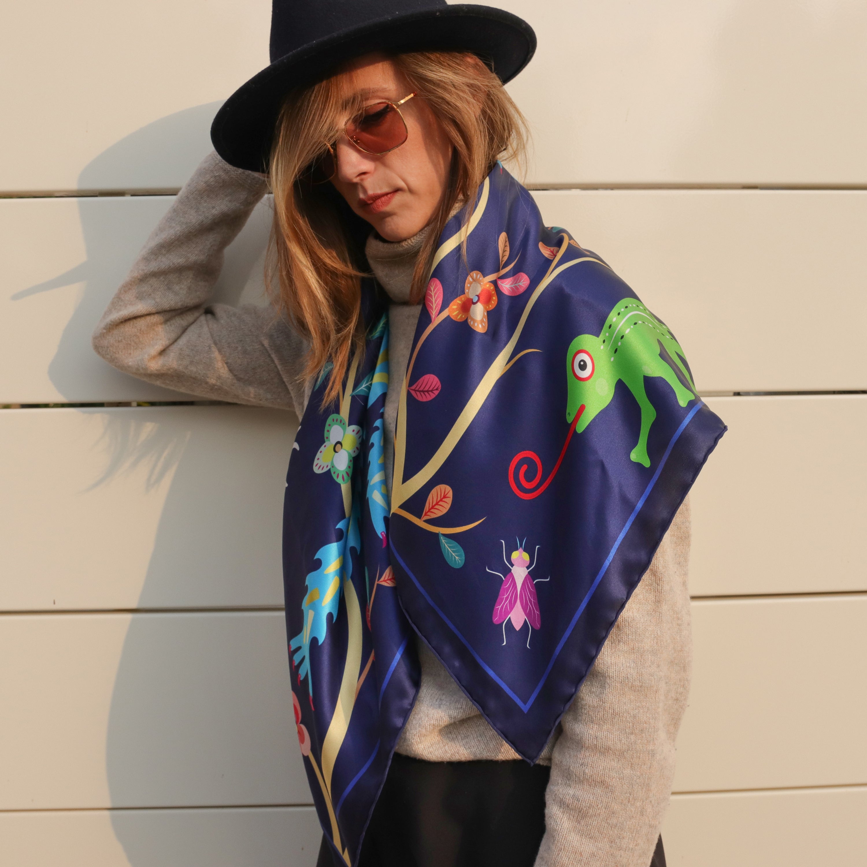 Model wearing the Abomey Indigo silk scarf draped over the shoulders with a grey sweater and black hat.