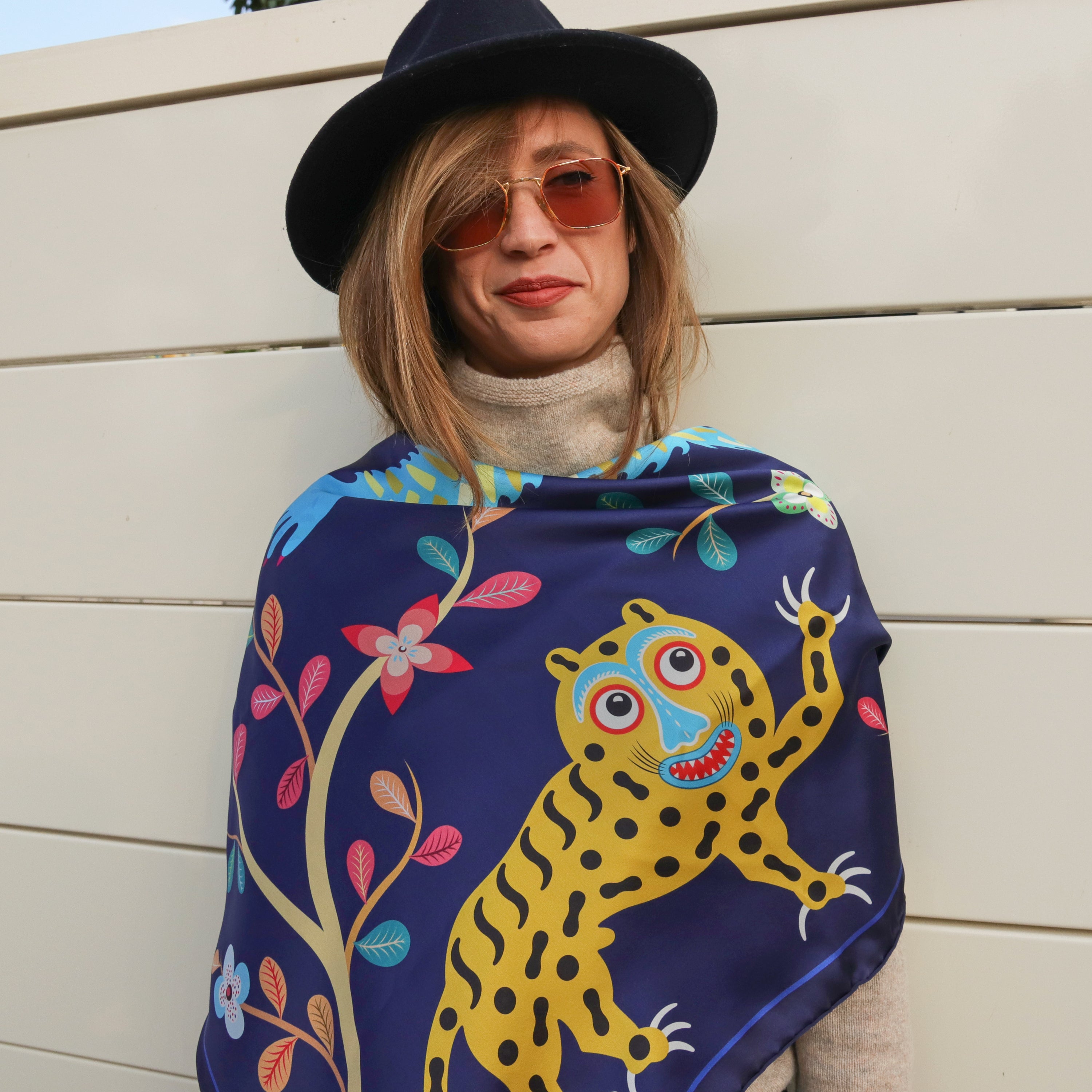 Model wearing the Abomey Indigo silk scarf draped over the shoulders with a grey sweater and black hat.