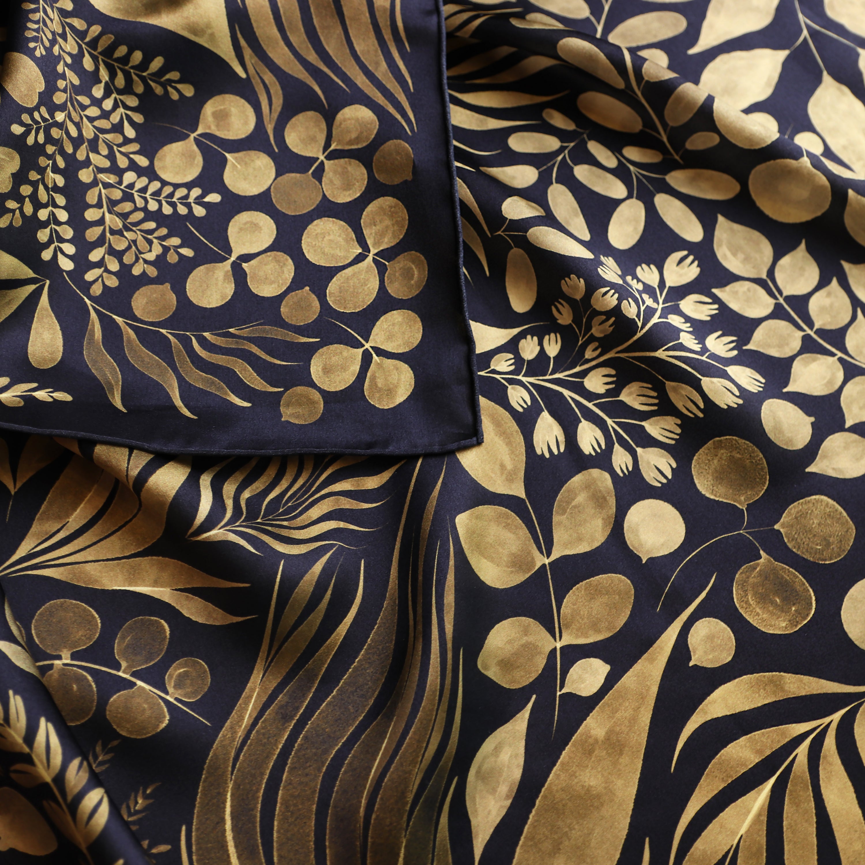 Detail of the Foglie d'Oro silk scarf showing hand-painted botanical leaf motifs and the hand-rolled hem.