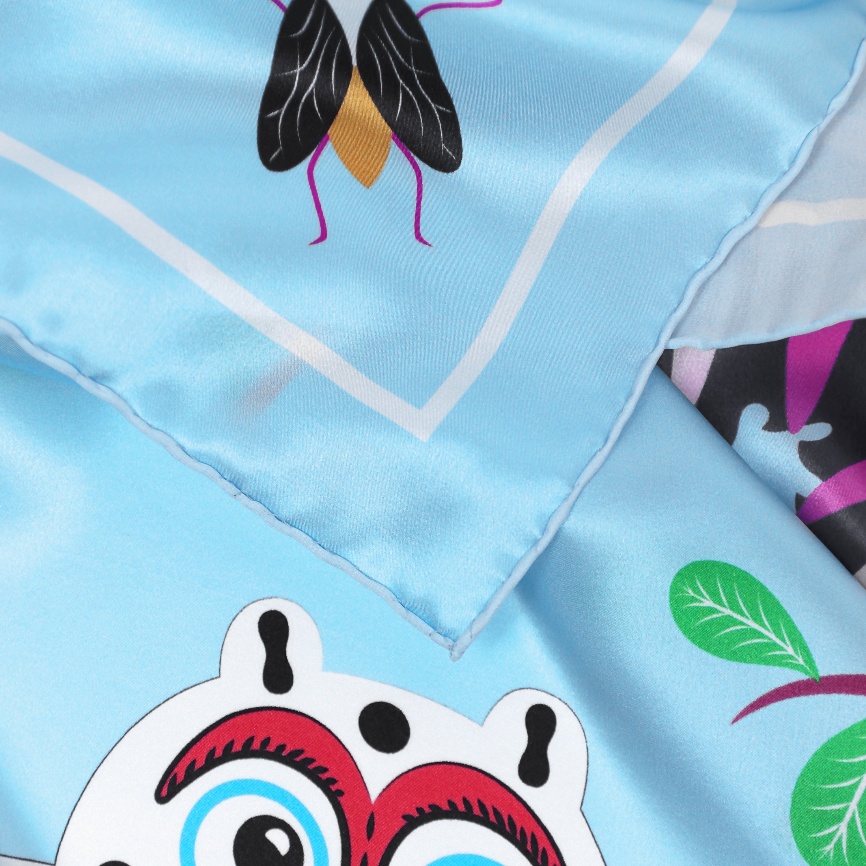 Detail of the Abomey Maya silk scarf showing hand-painted animal and botanical motifs and the hand-rolled hem.
