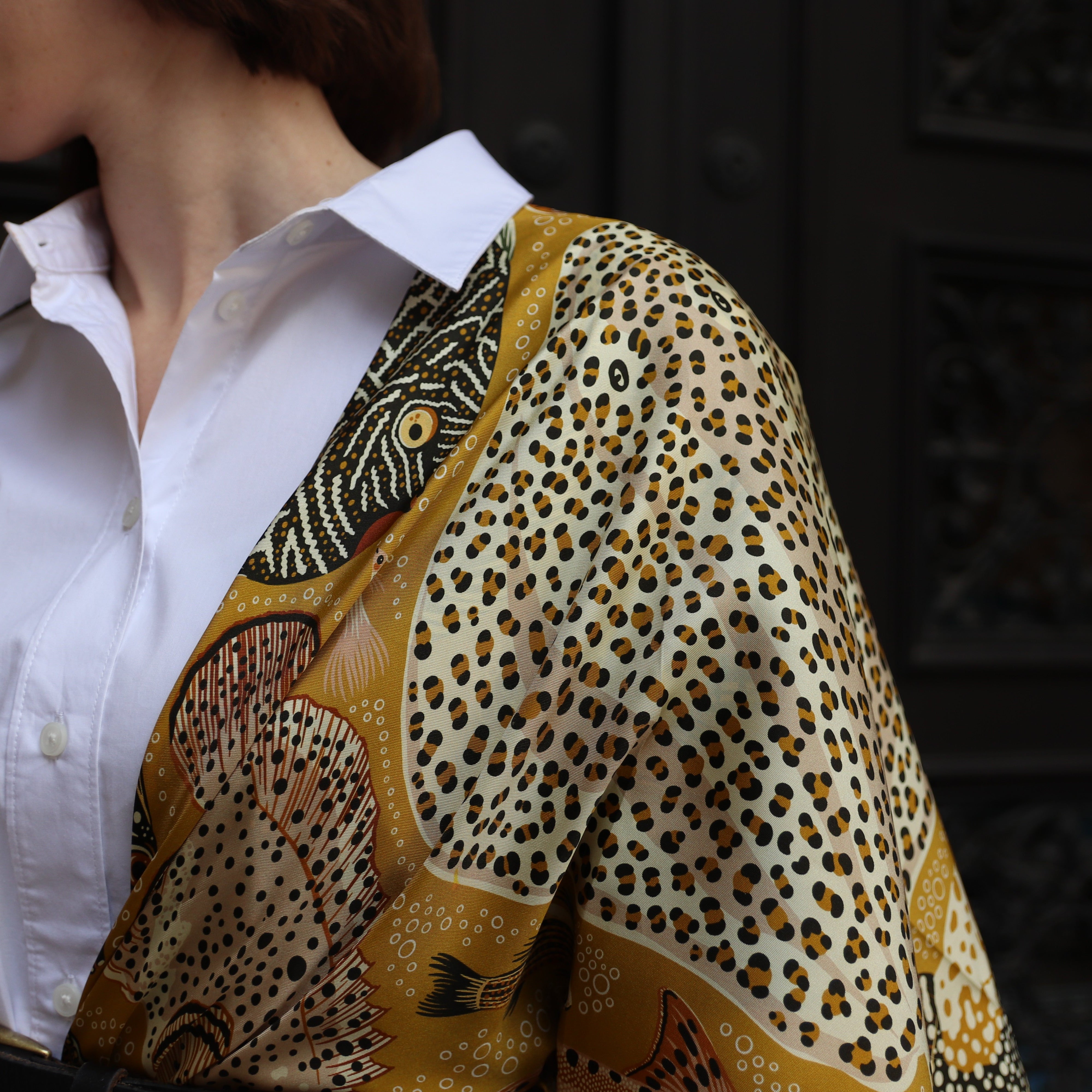 Close-up of the Pesce Miele double-sided silk scarf showing hand-painted fish motifs and contrasting pattern details on 100% silk twill.