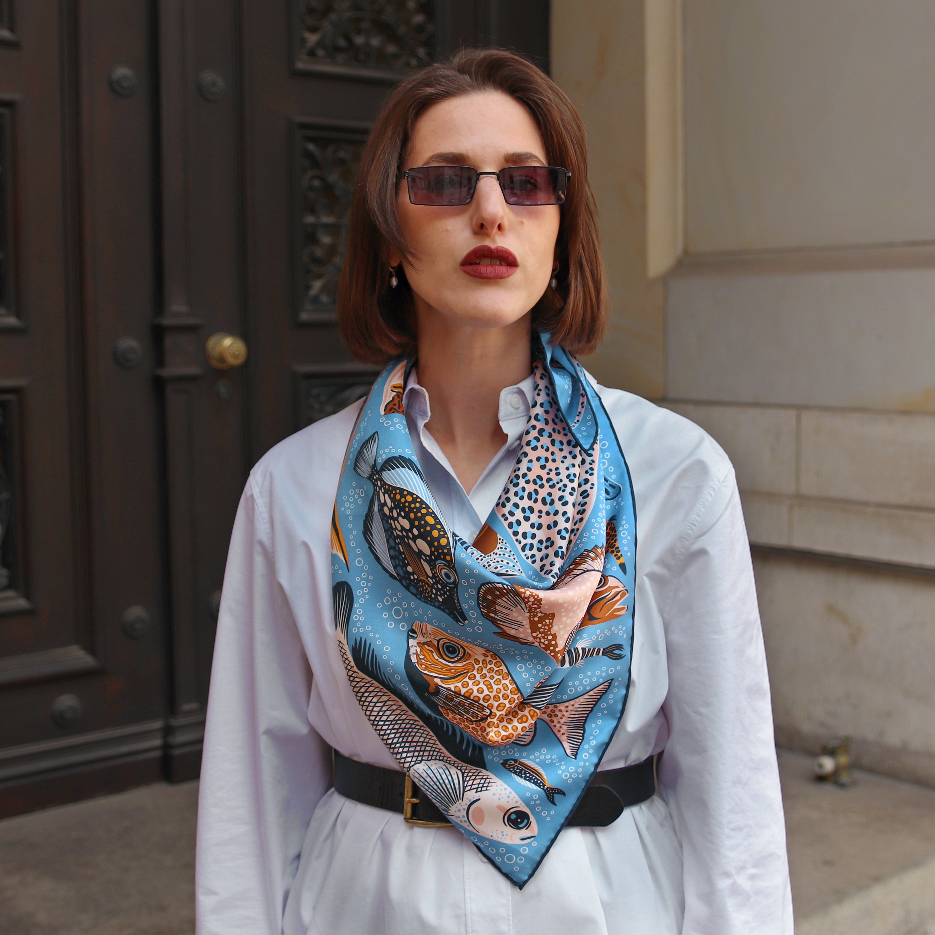 Model wearing the Pesce Iris double-sided silk scarf styled around the neck with a white shirt.