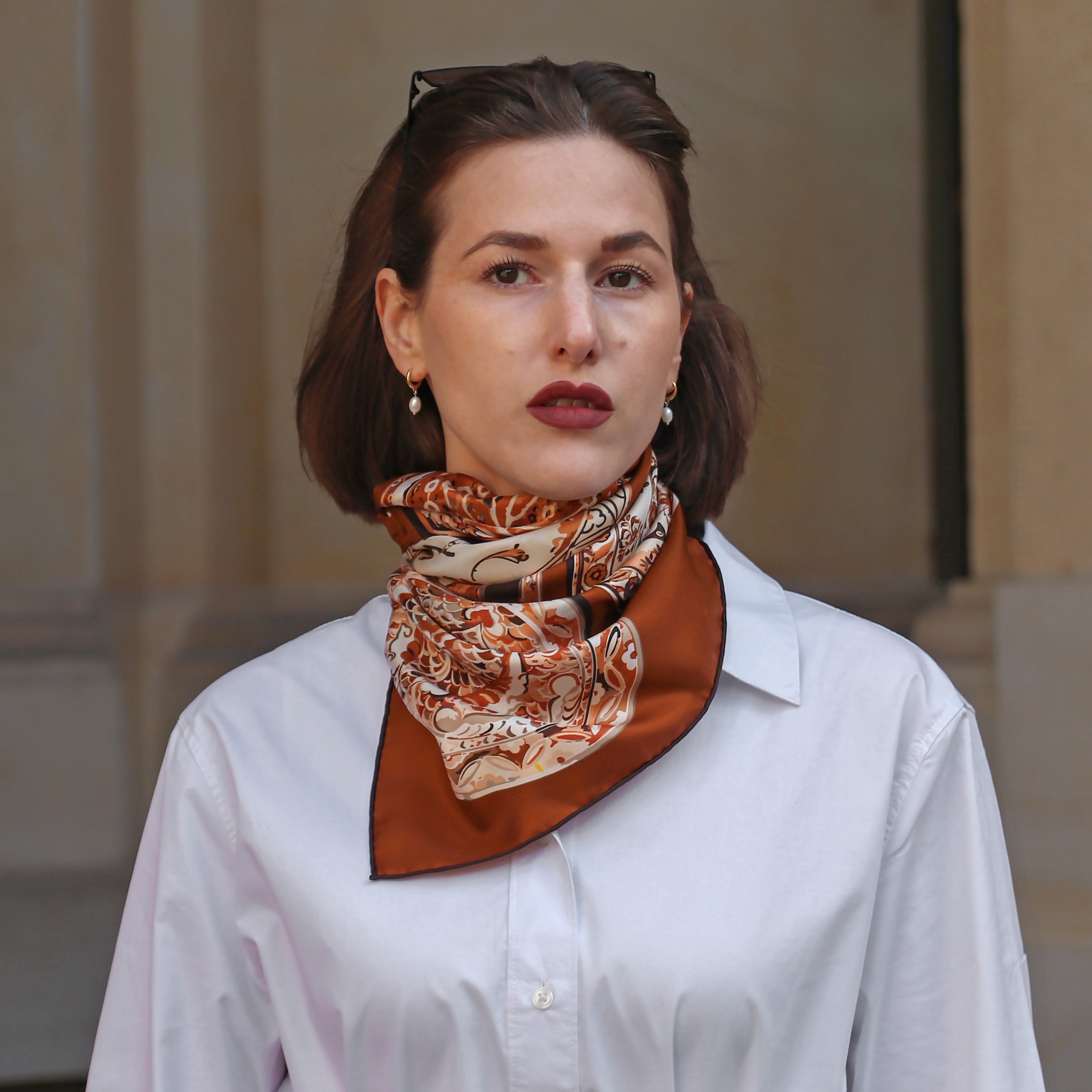 Model wearing the Iznik Chamoise double-sided silk scarf styled around the neck with a white blouse.