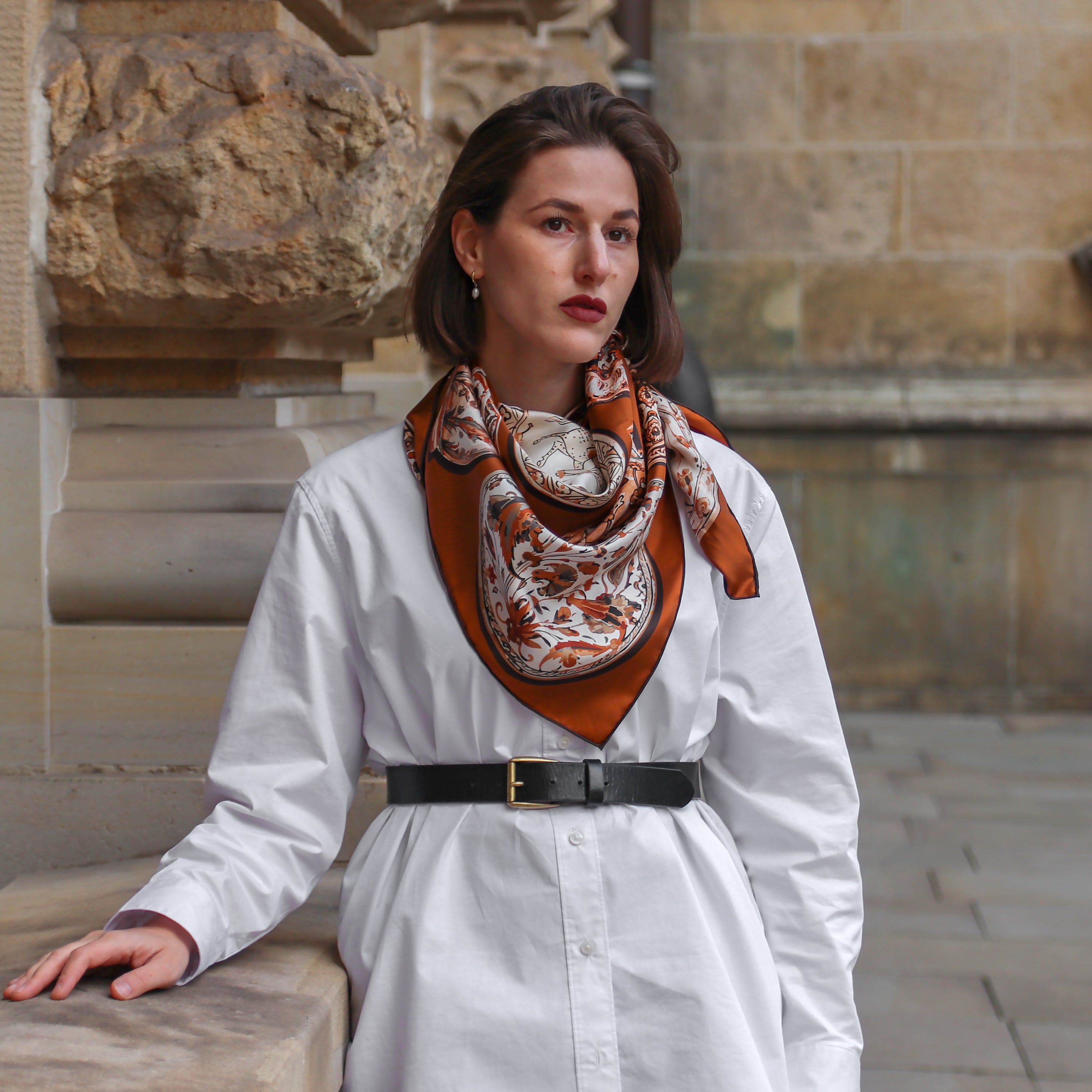 Model wearing the Iznik Chamoise double-sided silk scarf styled around the neck with a white dress.
