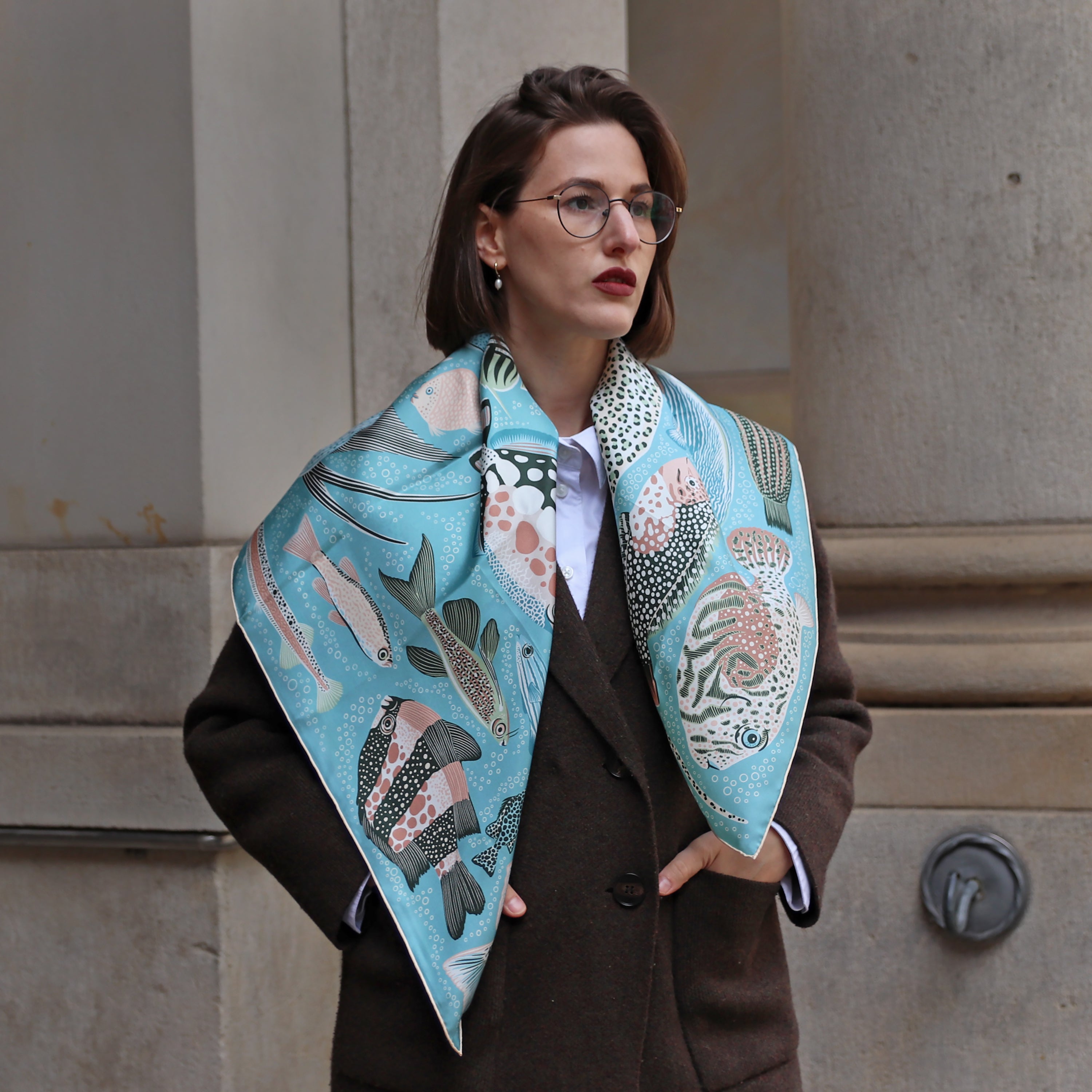 Model wearing the Pesce Acqua double-sided silk scarf draped over the shoulders with a dark coat.